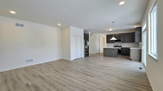 kitchen featuring decorative backsplash, hanging light fixtures, light hardwood / wood-style floors, and appliances with stainless steel finishes