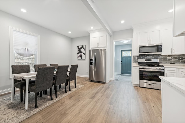 kitchen with white cabinets, appliances with stainless steel finishes, backsplash, and light hardwood / wood-style floors