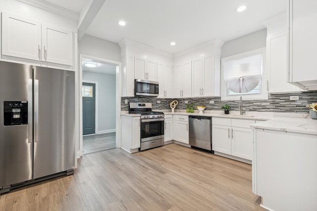 kitchen featuring decorative backsplash, stainless steel appliances, sink, light hardwood / wood-style flooring, and white cabinets