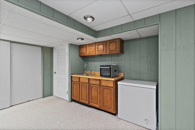 kitchen with a paneled ceiling, refrigerator, sink, and light carpet