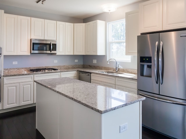 kitchen with light stone countertops, appliances with stainless steel finishes, sink, white cabinets, and a kitchen island