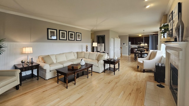 living room featuring a tile fireplace, crown molding, and light wood-type flooring