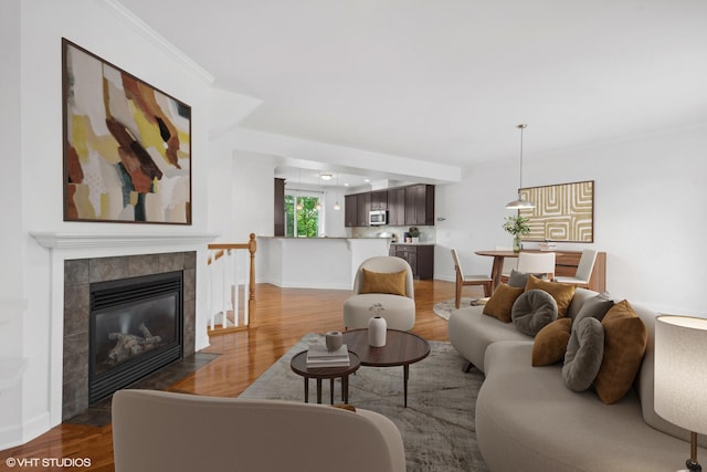 living room featuring a tiled fireplace, crown molding, and wood-type flooring