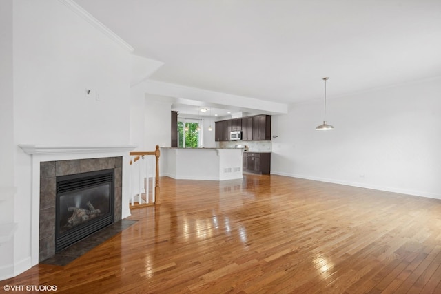 unfurnished living room with a tiled fireplace, crown molding, and wood-type flooring