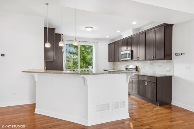 kitchen with a breakfast bar, pendant lighting, decorative backsplash, and light stone countertops