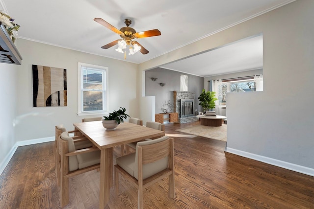 dining room with crown molding, a fireplace, baseboards, and wood finished floors