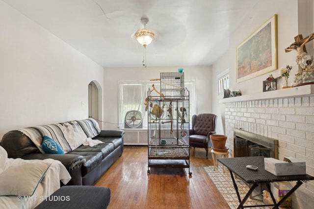 living room featuring hardwood / wood-style floors, radiator heating unit, a brick fireplace, and ceiling fan