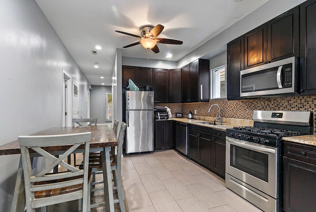 kitchen with tasteful backsplash, light stone counters, dark brown cabinets, stainless steel appliances, and sink