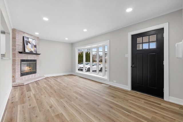 living room featuring light hardwood / wood-style flooring, ornamental molding, and a brick fireplace