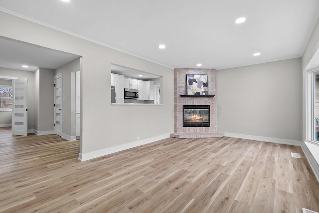 unfurnished living room with a fireplace, ornamental molding, and light wood-type flooring