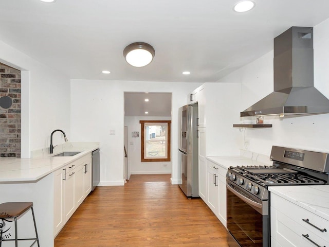 kitchen featuring light stone countertops, wall chimney range hood, appliances with stainless steel finishes, white cabinets, and light wood-type flooring