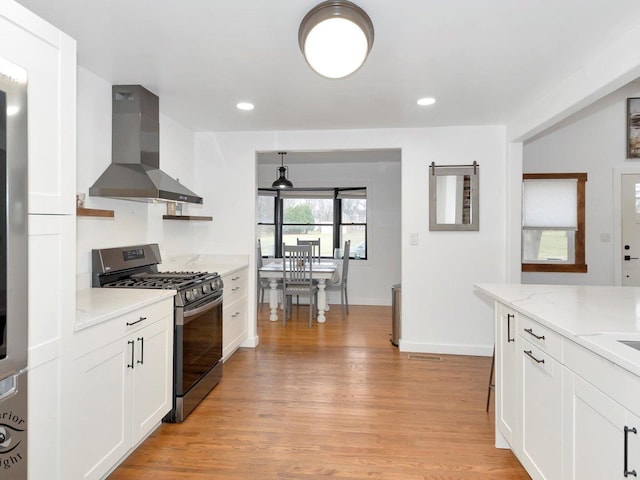 kitchen with black gas stove, wall chimney range hood, light wood-type flooring, decorative light fixtures, and white cabinetry