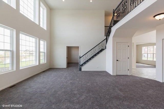 unfurnished living room featuring a towering ceiling and dark carpet