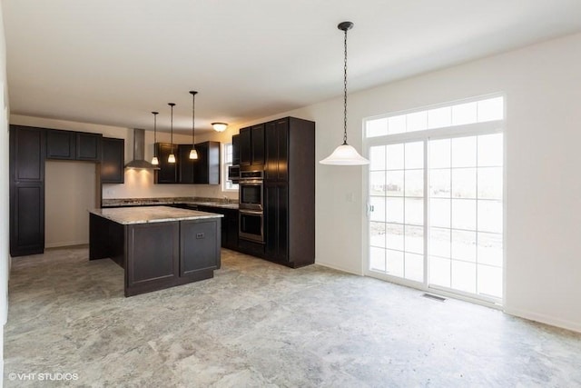 kitchen with pendant lighting, wall chimney exhaust hood, a center island, and light stone counters