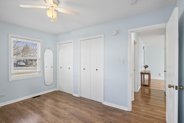 unfurnished bedroom featuring two closets, dark wood-type flooring, and ceiling fan