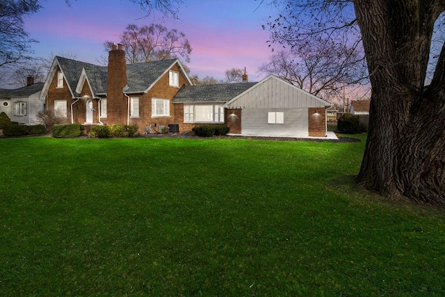 view of front of house featuring brick siding, a lawn, a chimney, and board and batten siding