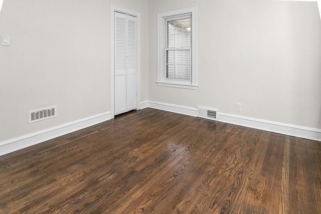 spare room with dark wood finished floors, visible vents, and baseboards