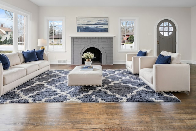 living area featuring arched walkways, a fireplace, visible vents, wood finished floors, and baseboards