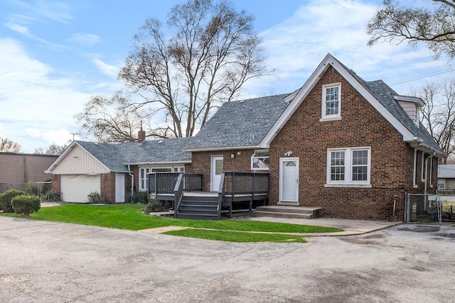 view of front of property featuring brick siding, a front yard, a wooden deck, and a shingled roof