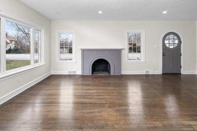 unfurnished living room featuring a brick fireplace, wood finished floors, visible vents, and baseboards