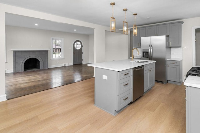 kitchen with gray cabinets, an island with sink, light hardwood / wood-style floors, and appliances with stainless steel finishes