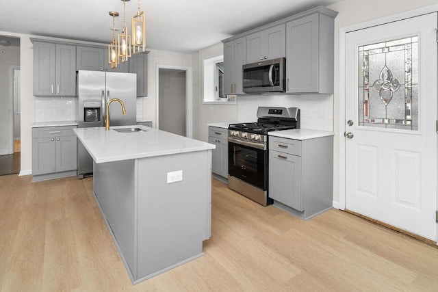 kitchen with tasteful backsplash, gray cabinetry, stainless steel appliances, sink, and an island with sink