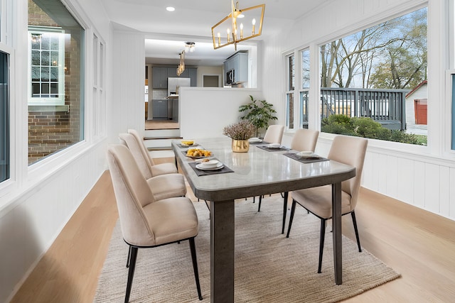 dining space with light wood finished floors, a decorative wall, recessed lighting, and an inviting chandelier