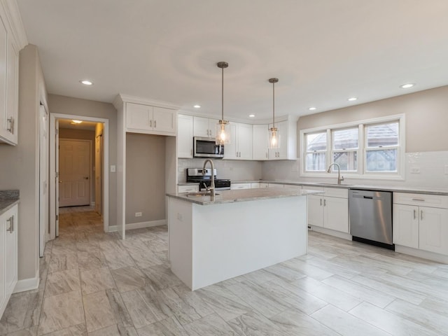 kitchen with white cabinetry, stainless steel appliances, light stone counters, decorative light fixtures, and a kitchen island with sink