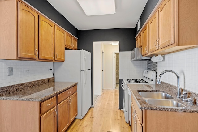 kitchen with white appliances, light wood-type flooring, dark stone counters, sink, and backsplash