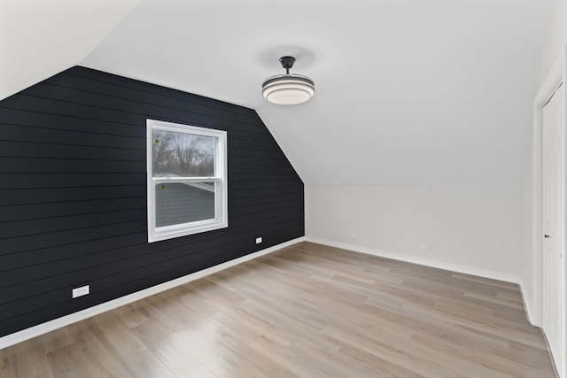 bonus room featuring wooden walls, light hardwood / wood-style flooring, and lofted ceiling