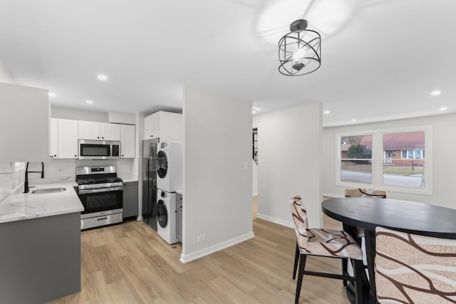 kitchen featuring sink, decorative light fixtures, appliances with stainless steel finishes, stacked washer and clothes dryer, and light wood-type flooring