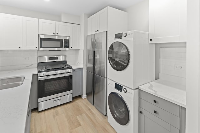 kitchen with white cabinets, stacked washing maching and dryer, appliances with stainless steel finishes, and light hardwood / wood-style flooring