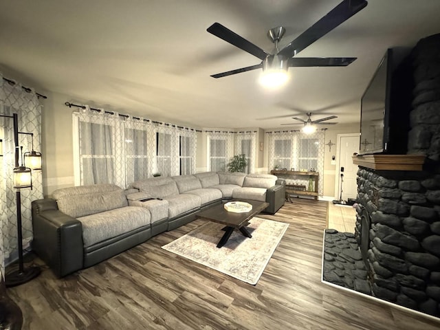 living room featuring ceiling fan, a fireplace, and wood finished floors