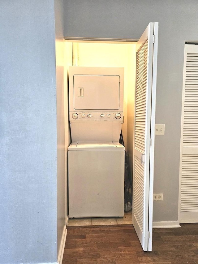 clothes washing area with dark hardwood / wood-style flooring and stacked washer / drying machine