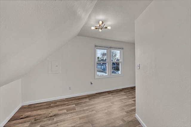 additional living space featuring a chandelier, hardwood / wood-style floors, a textured ceiling, and vaulted ceiling