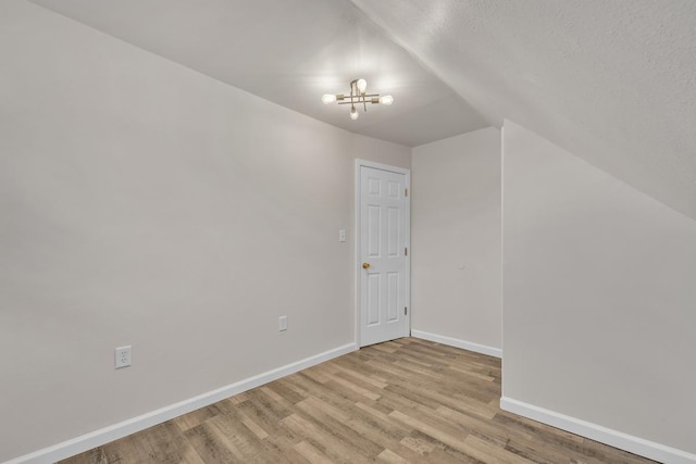 additional living space featuring a chandelier, light wood-type flooring, and vaulted ceiling