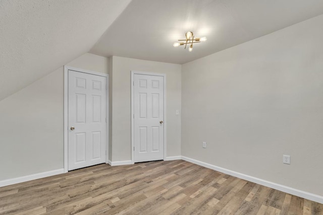 unfurnished bedroom featuring an inviting chandelier, vaulted ceiling, and light wood-type flooring