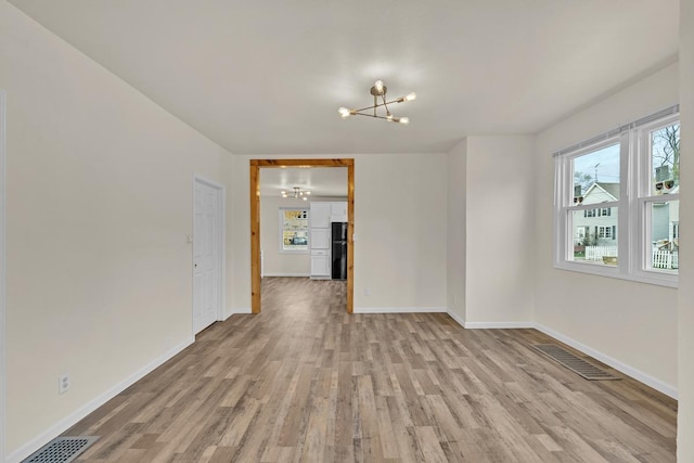 empty room featuring light wood-type flooring and a chandelier