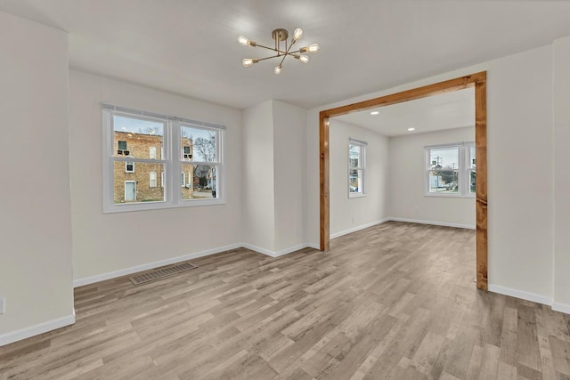 empty room with a notable chandelier and light hardwood / wood-style flooring