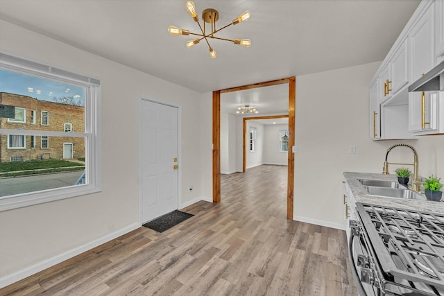 kitchen with stainless steel range with gas cooktop, sink, a notable chandelier, light hardwood / wood-style floors, and white cabinetry