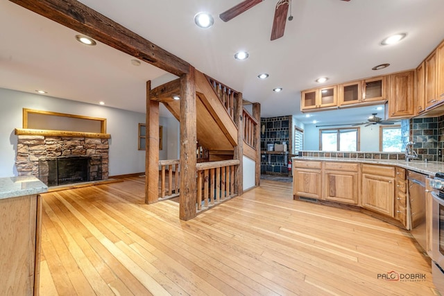 kitchen with a stone fireplace, light wood-type flooring, backsplash, and stainless steel range