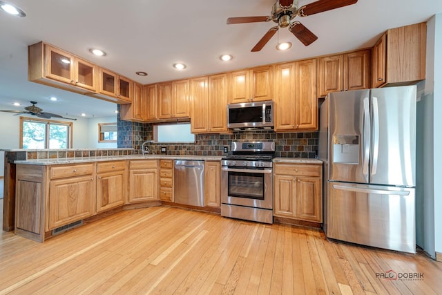 kitchen featuring ceiling fan, stainless steel appliances, backsplash, kitchen peninsula, and light wood-type flooring