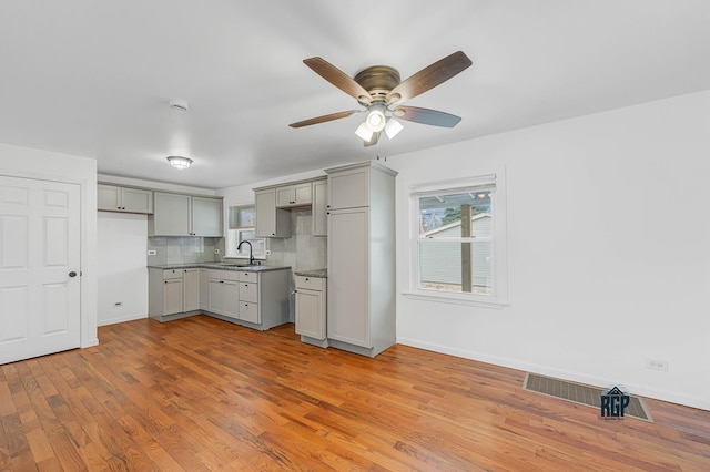 kitchen with ceiling fan, sink, light hardwood / wood-style flooring, backsplash, and gray cabinets