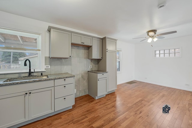 kitchen featuring ceiling fan, sink, stone countertops, light hardwood / wood-style flooring, and gray cabinets