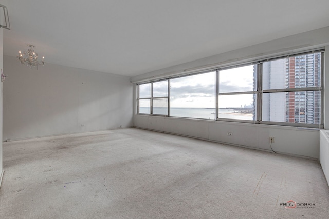 empty room with a water view, an inviting chandelier, and light carpet