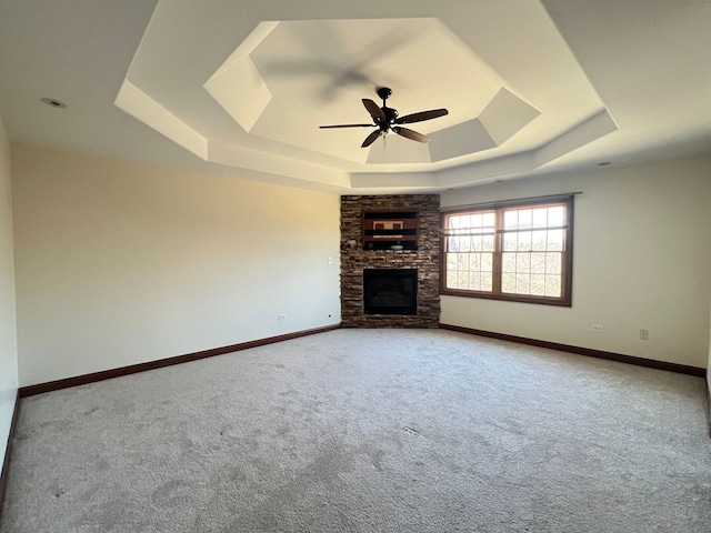 unfurnished living room with a tray ceiling, a stone fireplace, ceiling fan, and carpet flooring