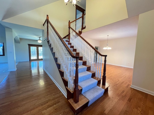 stairway featuring hardwood / wood-style floors, ceiling fan with notable chandelier, and french doors