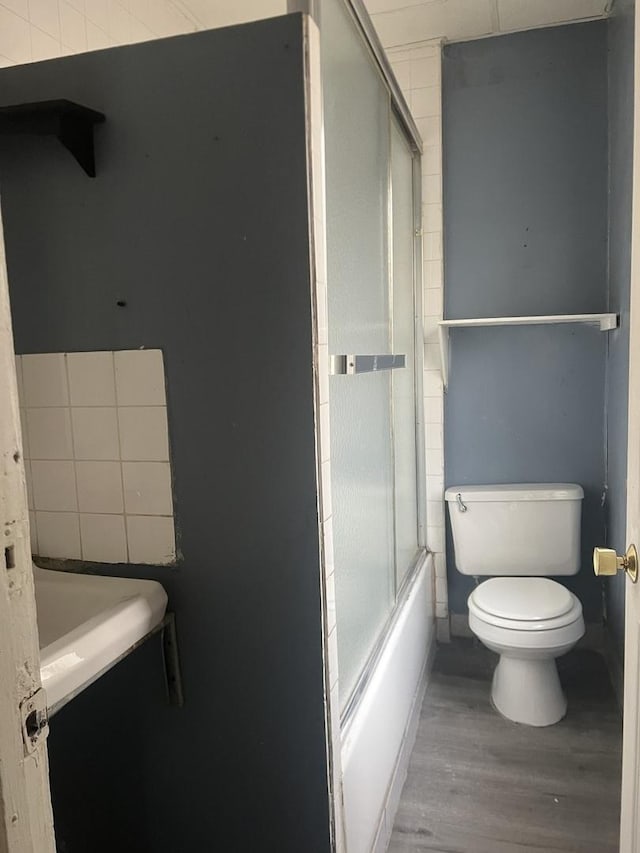 bathroom with toilet, bath / shower combo with glass door, and hardwood / wood-style flooring