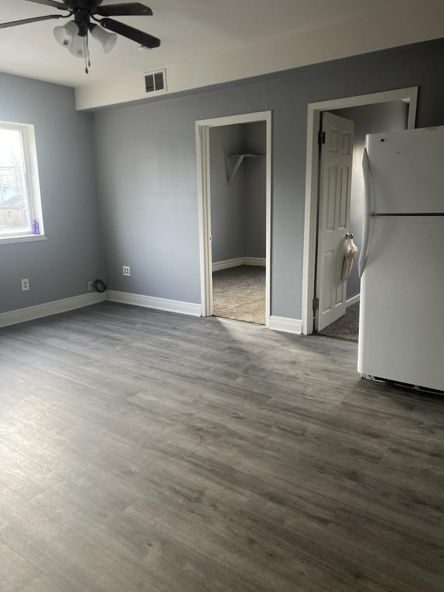 unfurnished bedroom featuring a walk in closet, wood-type flooring, white refrigerator, and ceiling fan