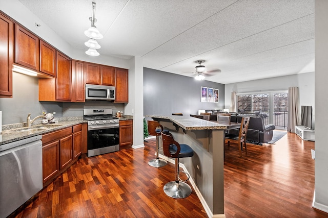 kitchen with appliances with stainless steel finishes, decorative light fixtures, light stone counters, and dark wood-type flooring